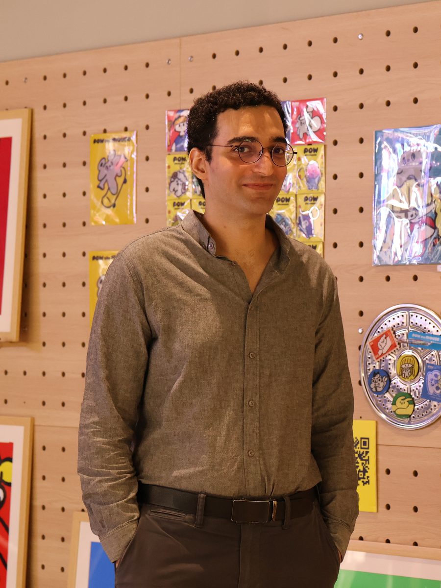 Benjamin Motahari standing in front of a colourful illustration gallery wall